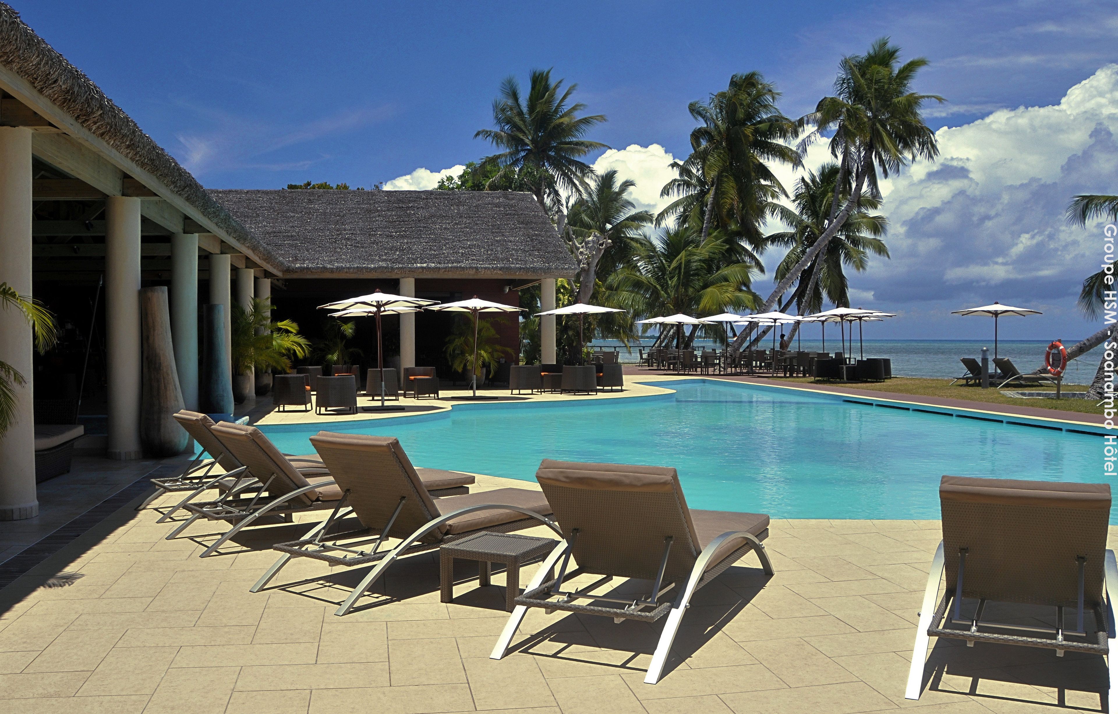 A poolside area with lounge chairs, umbrellas, and a building with a thatched roof.