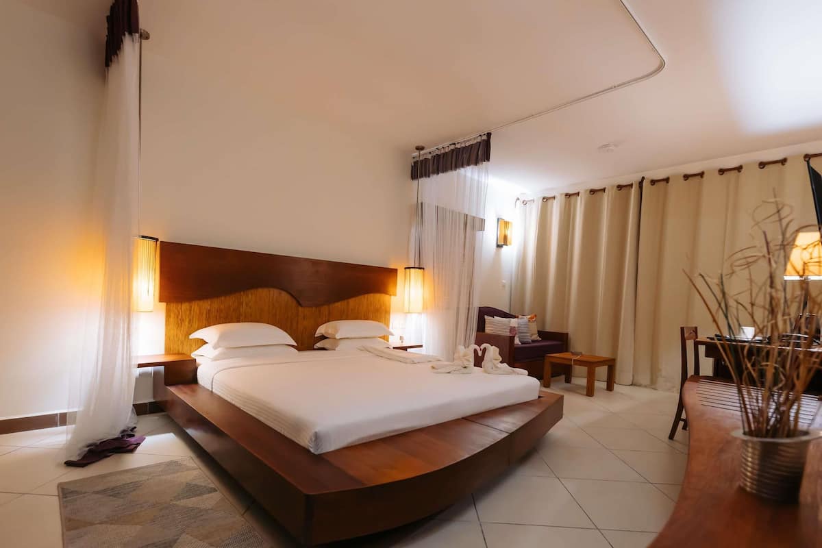 A hotel room with a large bed, bedside lamps, a small table, a chair, and a desk with a lamp.