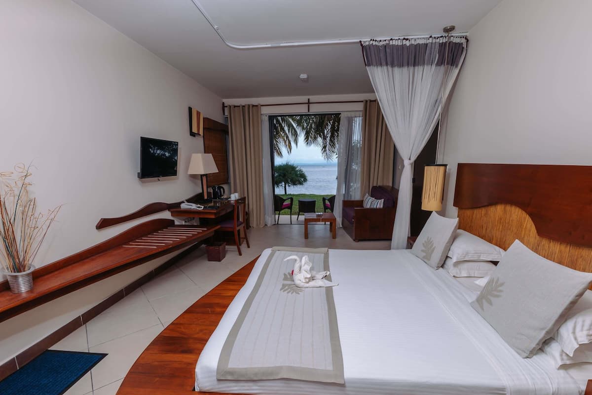 A hotel room with a bed, a desk, a chair, a TV, and a view of the sea.