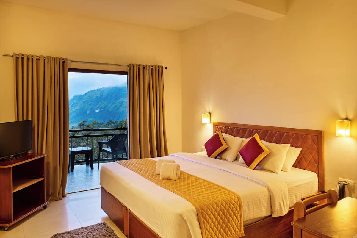 A hotel room with a bed, a TV, a table, and a view of the mountains.