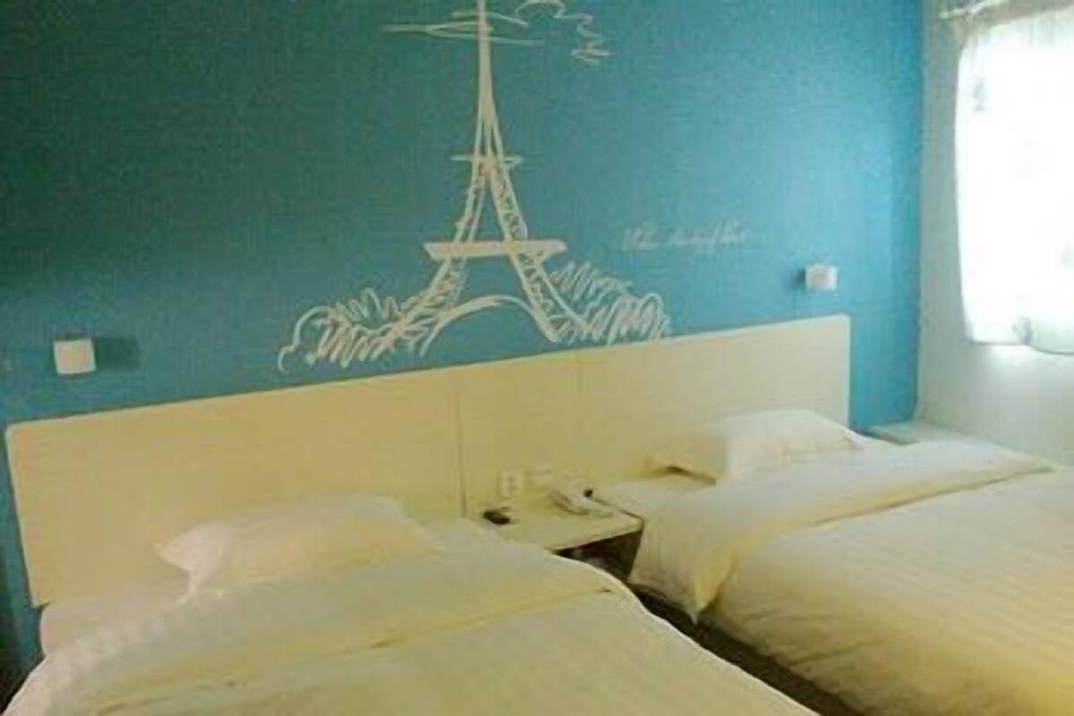 Habitación de hotel con dos camas, un mural de la Torre Eiffel y una ventana con cortinas.