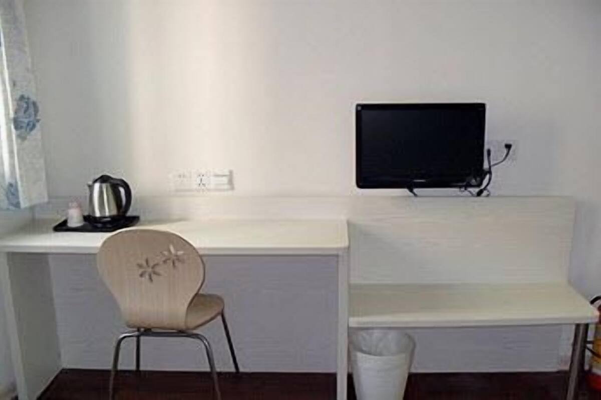 Una habitación pequeña y limpia con un escritorio blanco, una silla, un televisor y un cubo de basura.