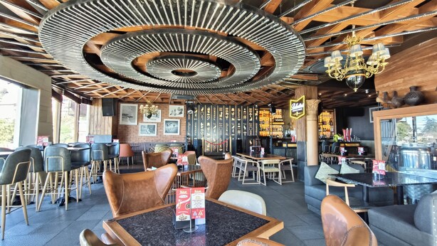 A restaurant with a modern interior, featuring a unique ceiling design, wooden tables, and chairs. - Bridge View Regency (Shimla)