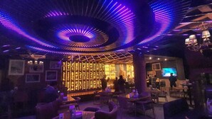 A dimly lit bar area with a spiral light installation on the ceiling, tables, and chairs arranged for patrons. - Bridge View Regency (Shimla)
