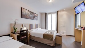 A hotel room with a bed, a desk, a chair, a TV, and a window. - Source Hotel (Paris)