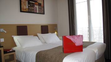 A hotel room with a large bed, a bedside table, a nightstand, a wall-mounted painting, and a window with curtains.