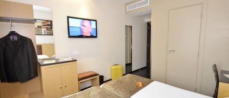 Una habitación de hotel con cama, escritorio, televisor, armario y maleta.