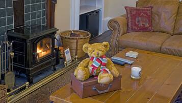 A cozy living room with a fireplace, a brown leather sofa, a coffee table with a teddy bear and a remote control, and a wicker basket.