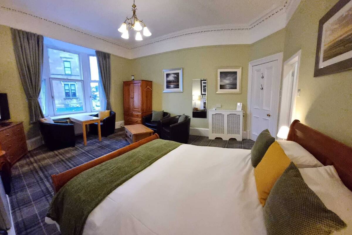 A hotel room with a bed, a desk, a chair, a wardrobe, and a window with a view of buildings.