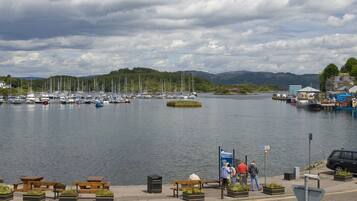 Un port de plaisance avec des bateaux amarrés, une promenade piétonne bordée de bancs et une vue sur des collines en arrière-plan.
