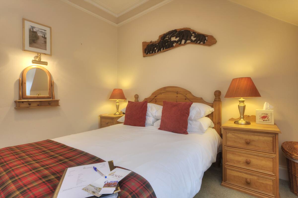 A neatly made bed with a plaid blanket, two bedside lamps, a wooden headboard, a mirror, and a wall-mounted decoration.