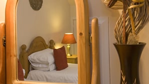 A bedroom with a wooden headboard, a bed with white bedding and red pillows, a bedside lamp, and a mirror reflecting the room. - Knap Guest House (Tarbert)