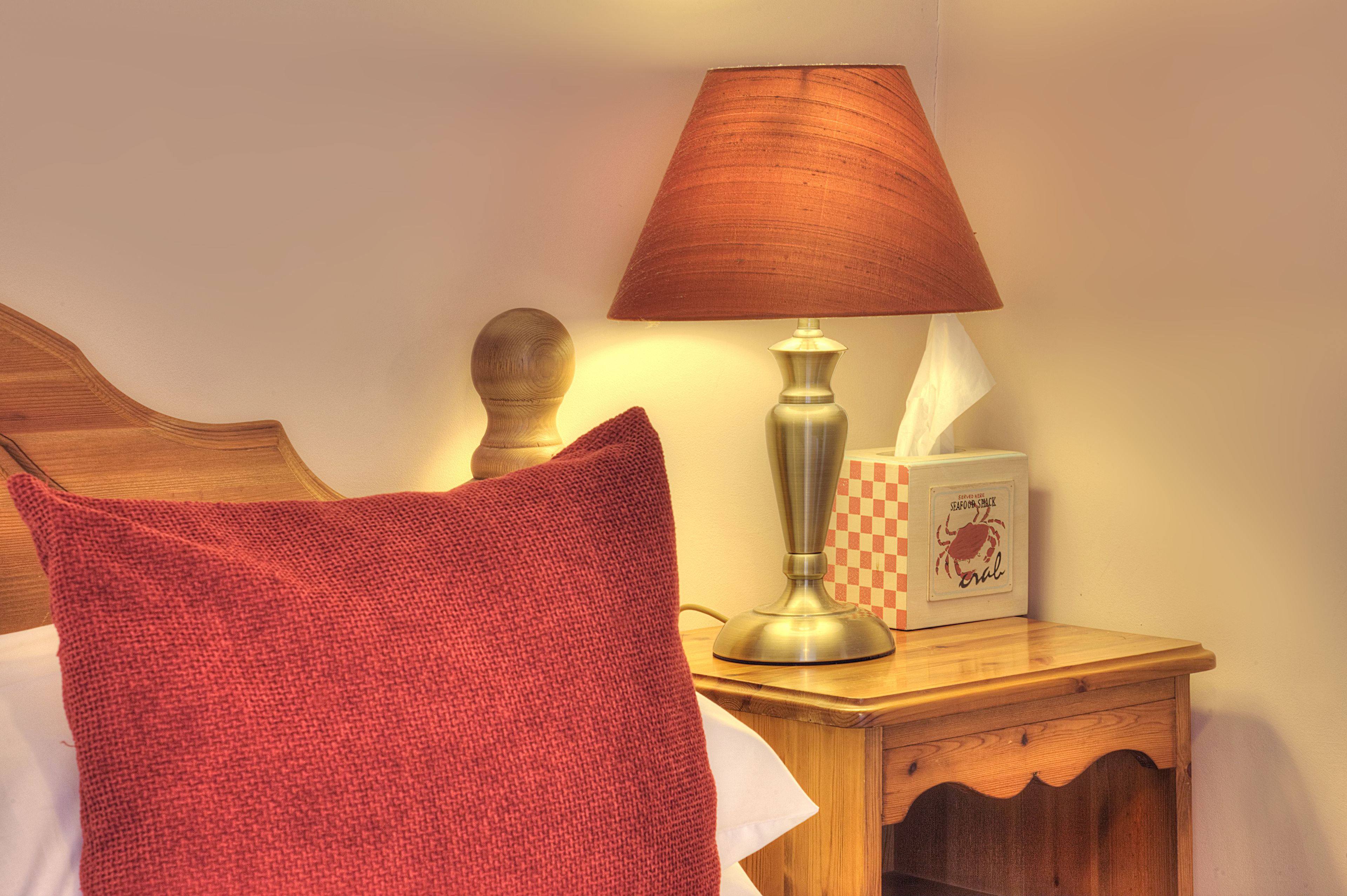A neatly made bed with a red pillow, a bedside lamp, and a tissue box on a wooden nightstand.