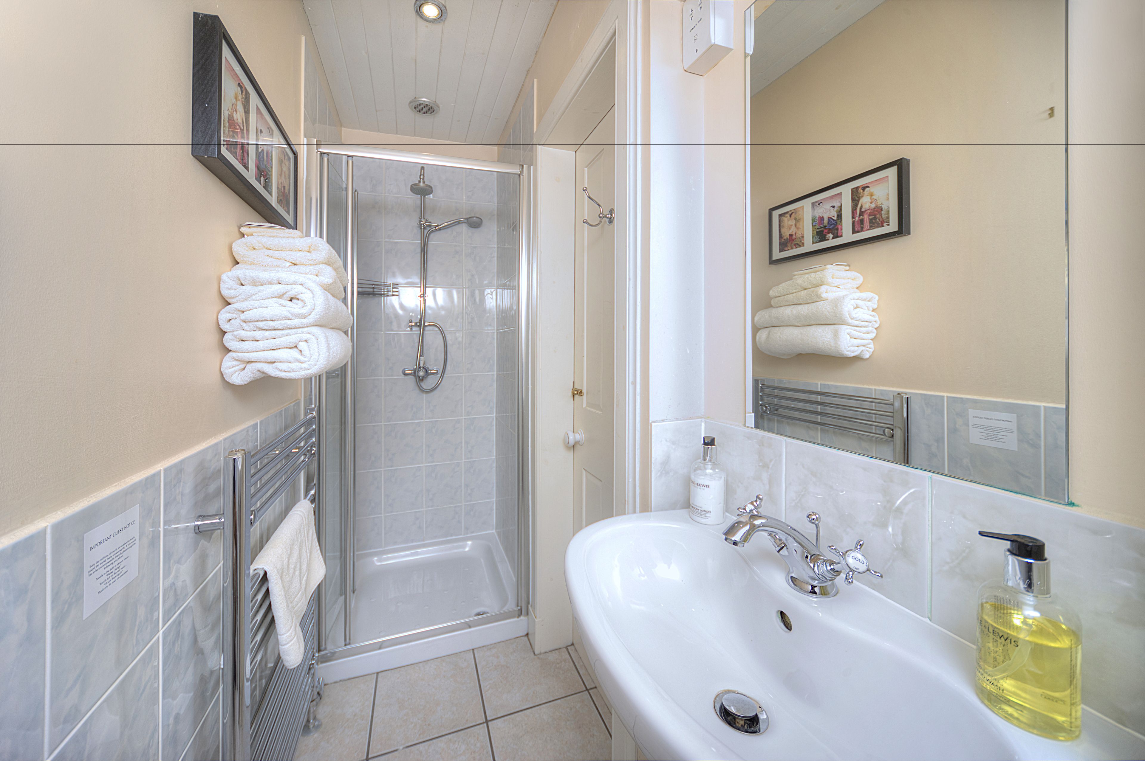 A bathroom with a glass-enclosed shower, a white sink with a mirror, and neatly stacked towels.