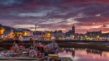 A harbor at dusk with boats docked, a prominent church tower, and buildings with illuminated signs.