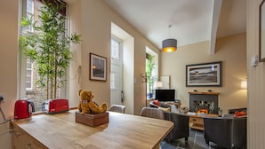A modern kitchen with a wooden countertop, a red toaster, and a teddy bear. There is a dining area with a table and chairs, and a living room with a sofa and a fireplace. - Knap Guest House (Tarbert)
