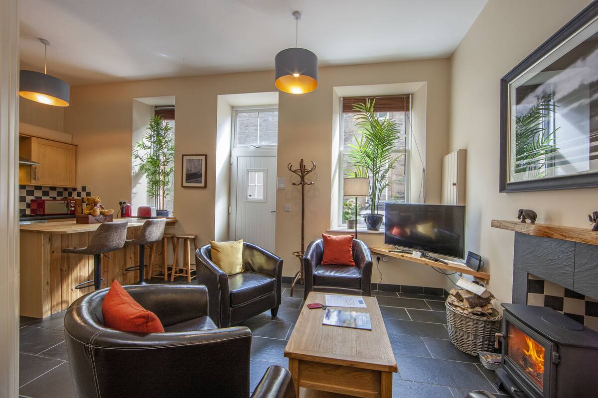 A modern living room with a fireplace, comfortable seating, a television, and a kitchen area with bar stools.