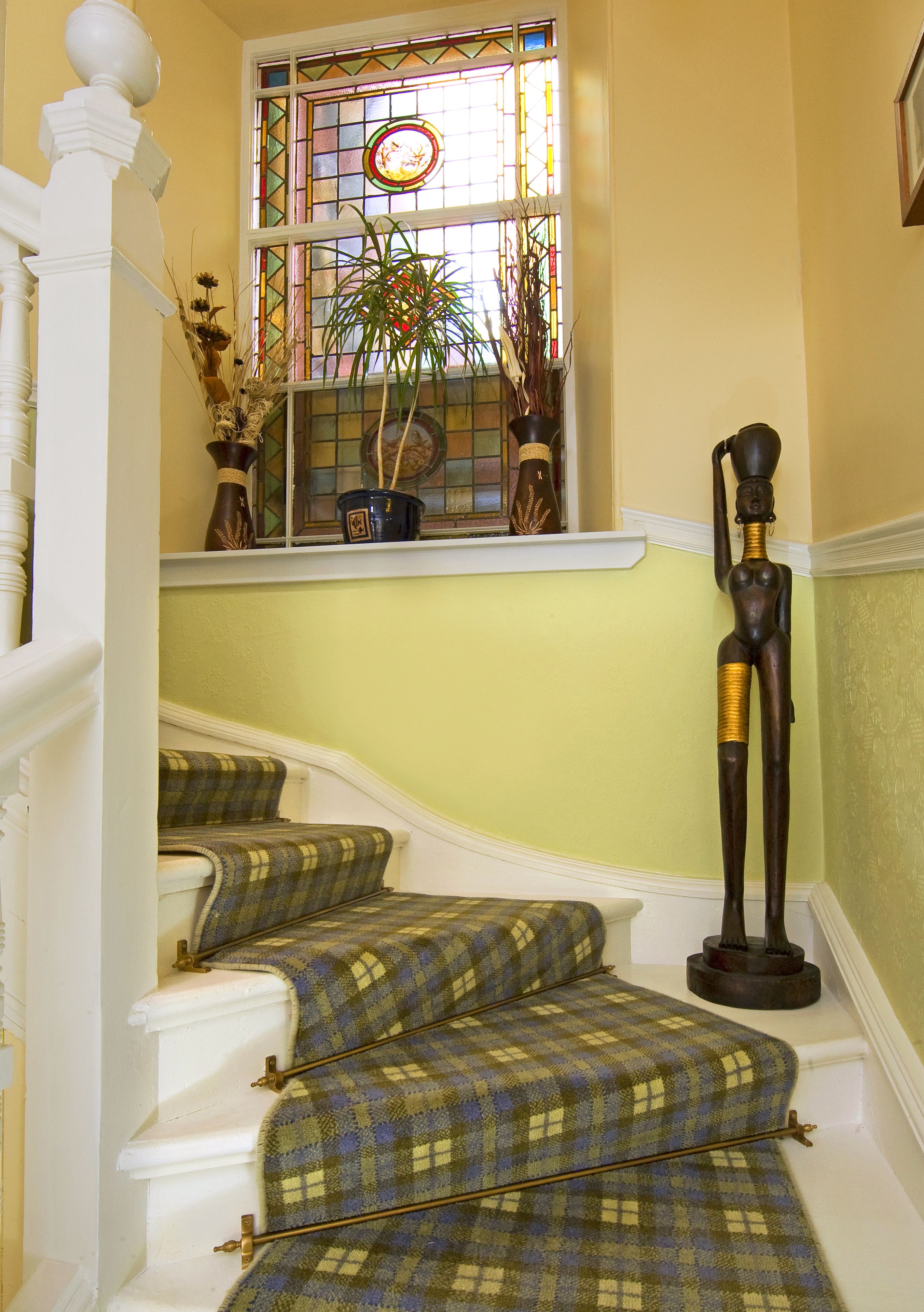 A staircase with plaid carpeted steps, a stained glass window, and a statue.
