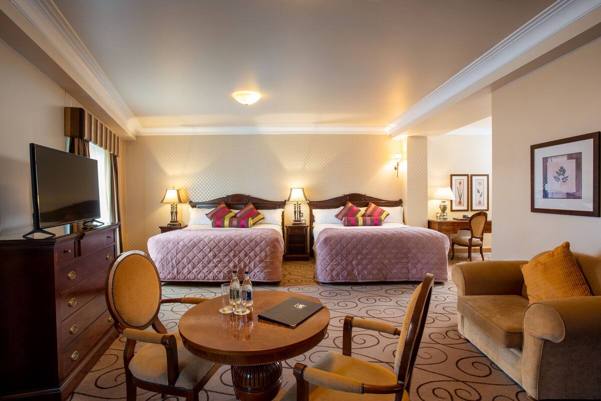 A hotel room with two beds, a TV, a dining table, and a sofa.
