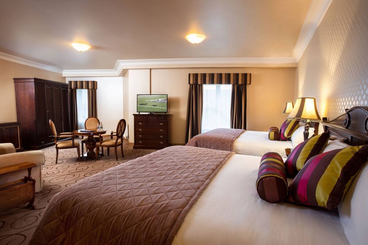 A hotel room with two beds, a television, a desk with chairs, and a wardrobe.