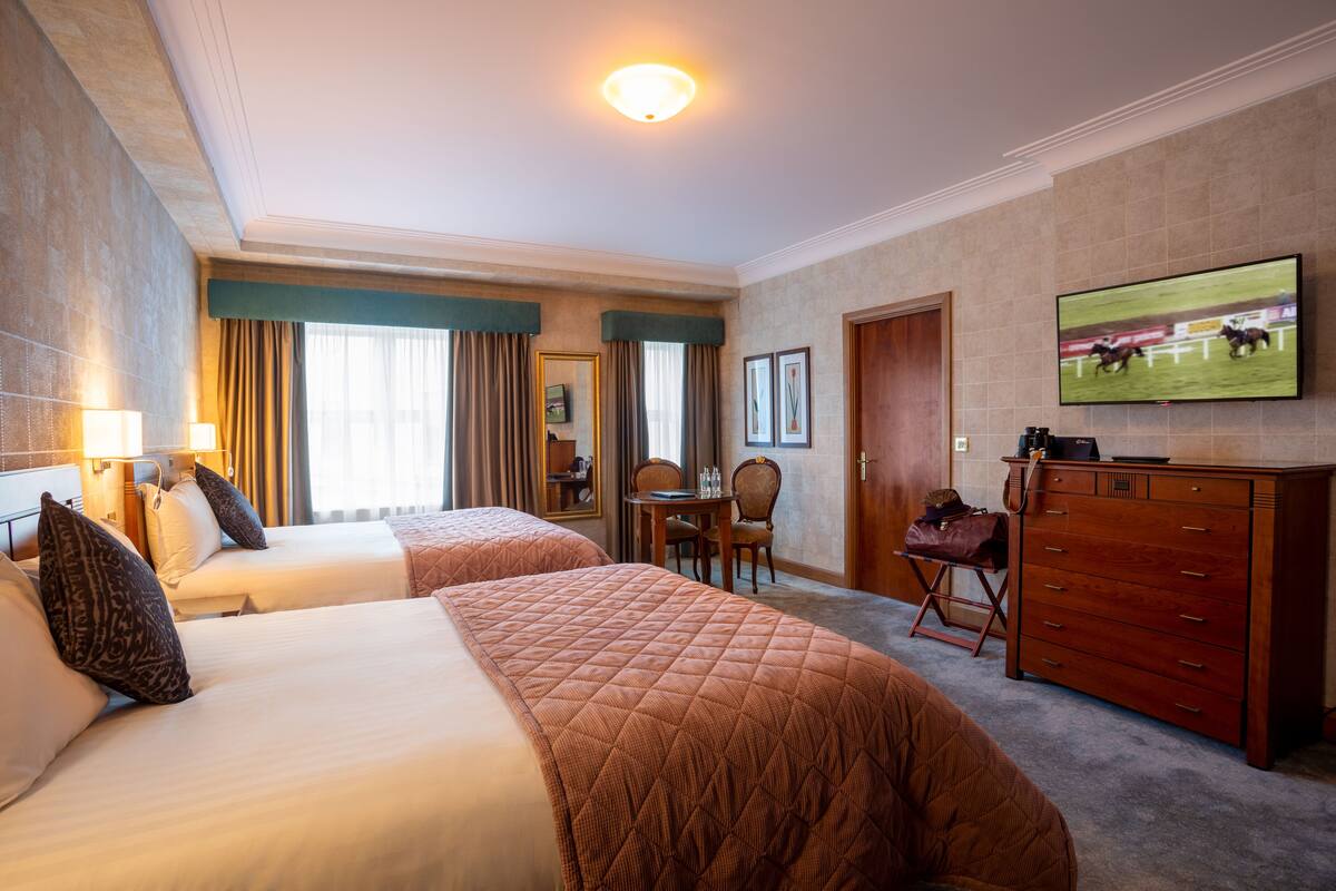 A hotel room with two beds, a television, a dresser, and a desk with a chair.