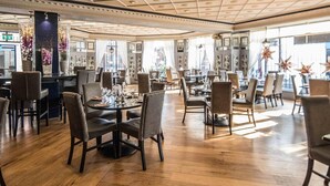 Un comedor amplio con varias mesas y sillas, piso de madera y elementos decorativos como jarrones y adornos con forma de estrella.