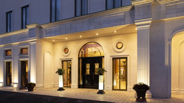 Imponente entrada de hotel con un amplio arco, columnas y plantas en macetas.