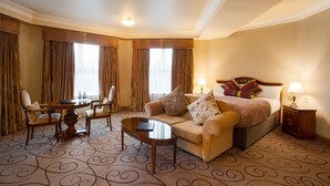 Una habitación de hotel con una cama, dos sillones, una mesa de centro y una mesita con botellas.