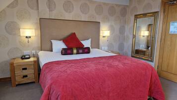 A hotel room with a large bed, a wooden nightstand, a mirror, and a wardrobe.