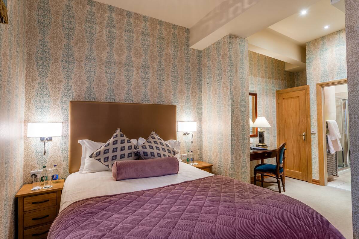 A hotel room with a large bed, a desk, a chair, and a wardrobe.
