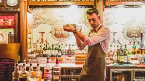 Un bar con un cantinero preparando una bebida, estantes llenos de botellas de licor y un letrero antiguo que dice "LAWLOR'S EST. 1913".