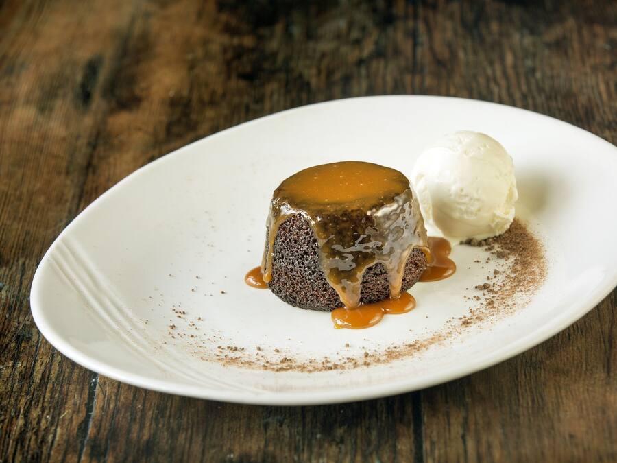 A dessert on a white plate with caramel sauce and a scoop of ice cream.