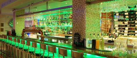 Una zona de bar con una barra larga, distintas opciones de asientos y una variedad de botellas y copas a la vista.