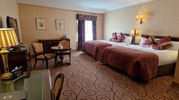 A hotel room with two beds, a desk with a chair, a small table, and a lamp.