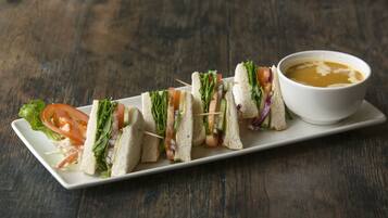 Un plato blanco rectangular con varios pinchos de sándwich y un bol de sopa sobre una mesa de madera.