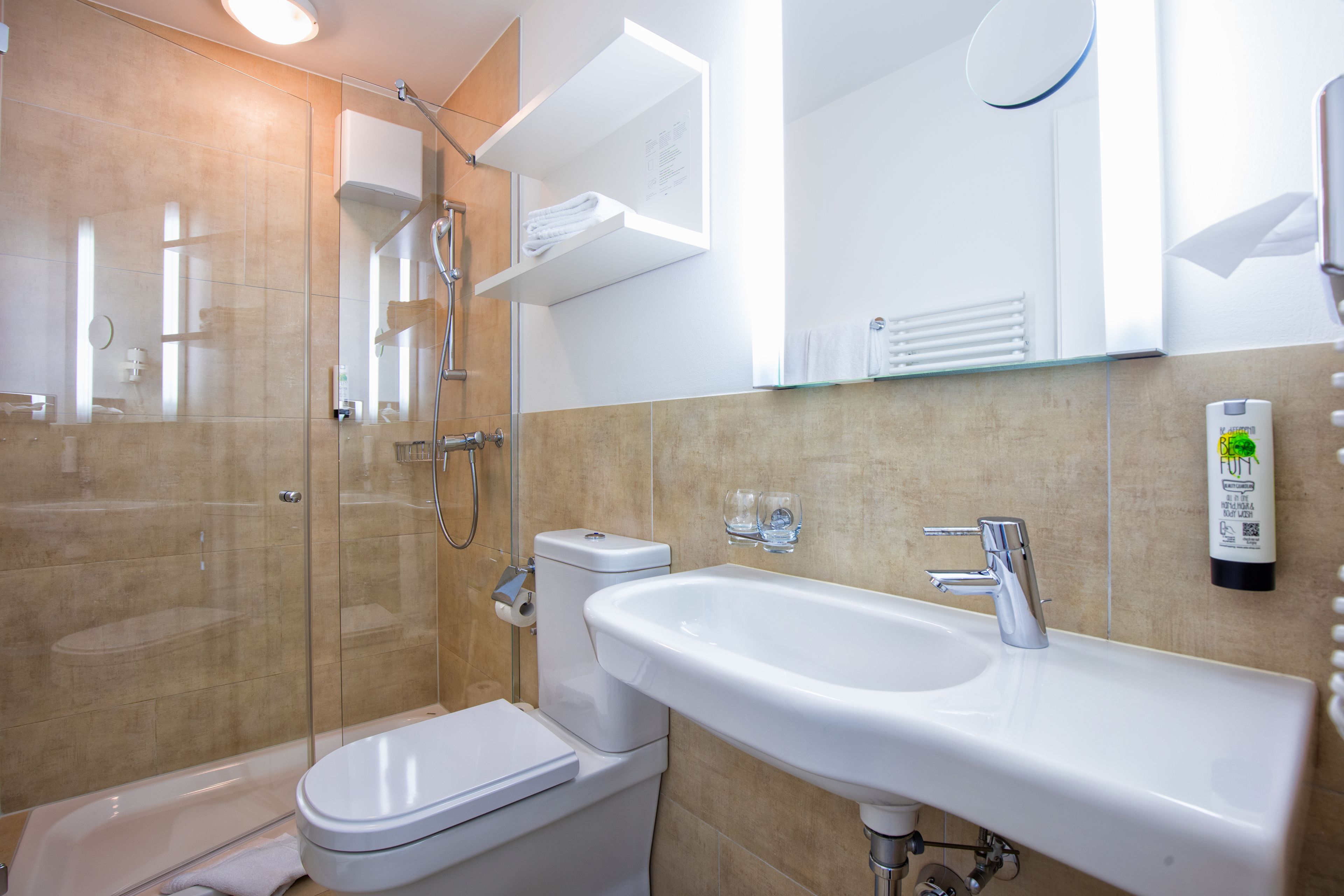Un baño moderno con ducha de vidrio, inodoro blanco y lavabo con espejo superior.