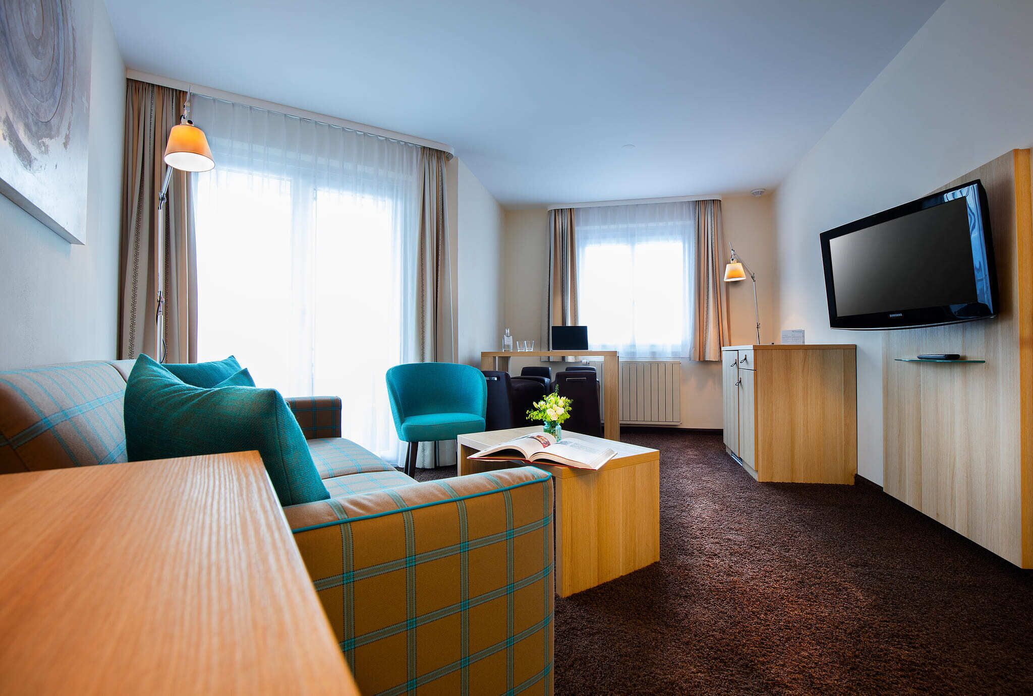 Habitación de hotel con sofá, una mesita con un libro, televisor y escritorio con silla.