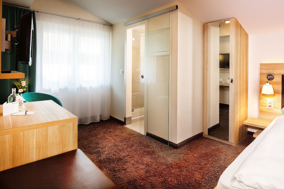 A hotel room with a bed, a desk, a chair, a wardrobe, and a bathroom.