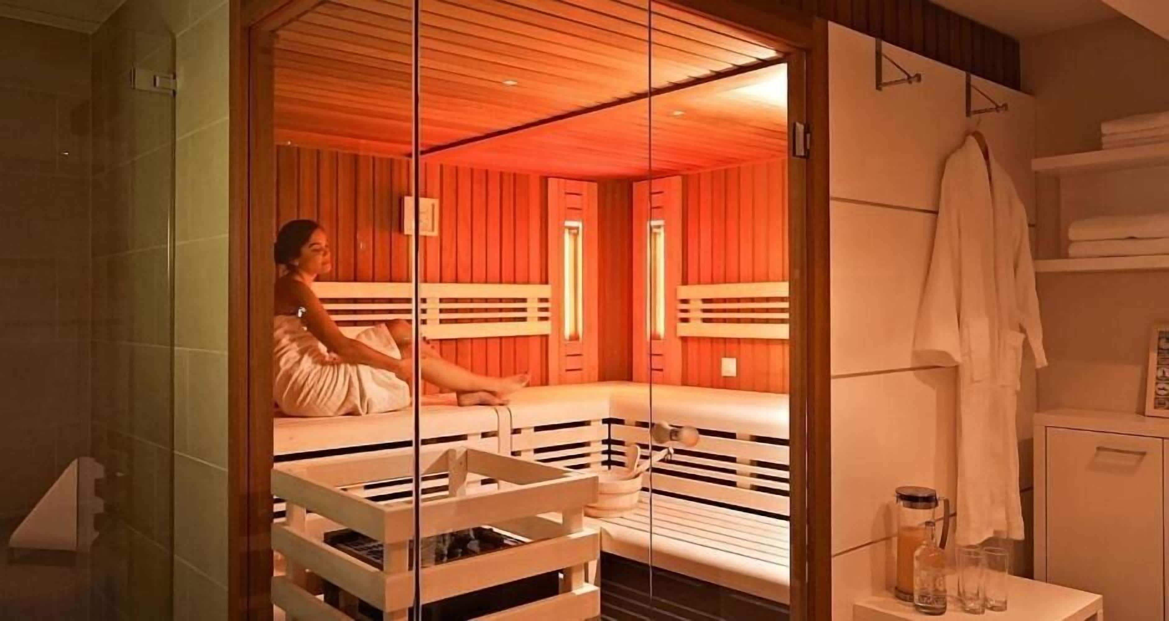 A room with a glass partition, wooden benches, and a white cabinet with towels.
