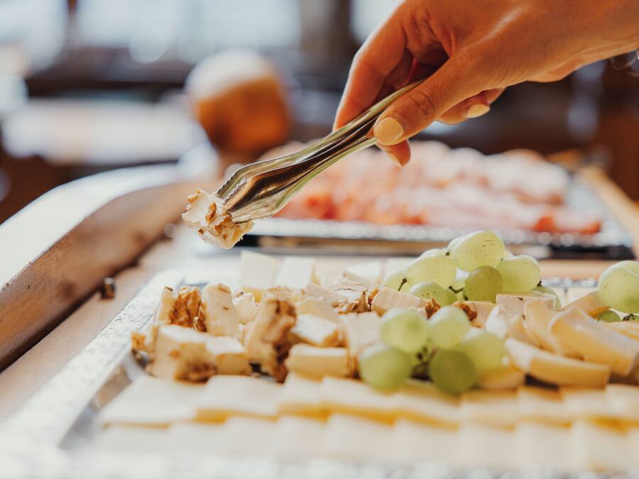A hand holding tongs over a tray of food, including cheese and grapes.