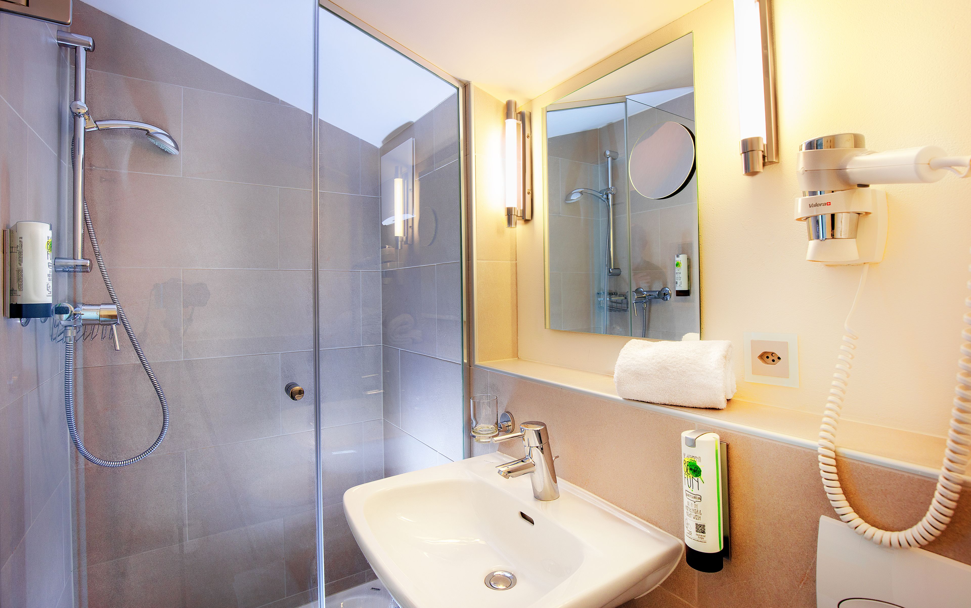 A modern bathroom with a glass-enclosed shower, a sink with a soap dispenser, and a mirror above the sink.