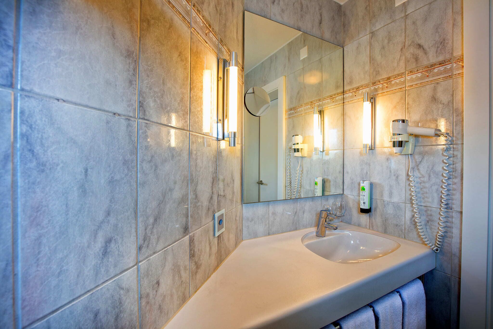 Une salle de bain avec un grand miroir, un lavabo et un sèche-cheveux fixé au mur.