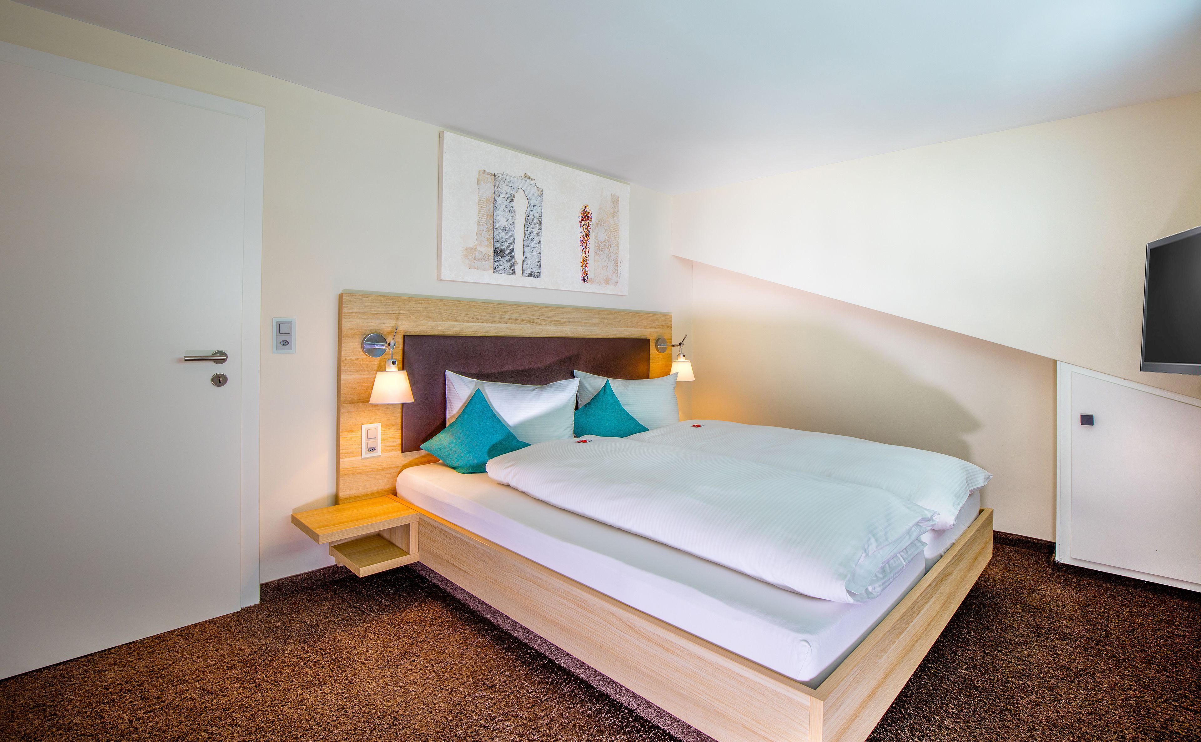 A neatly made bed with a wooden headboard, two bedside lamps, and a small wooden nightstand with a lamp.