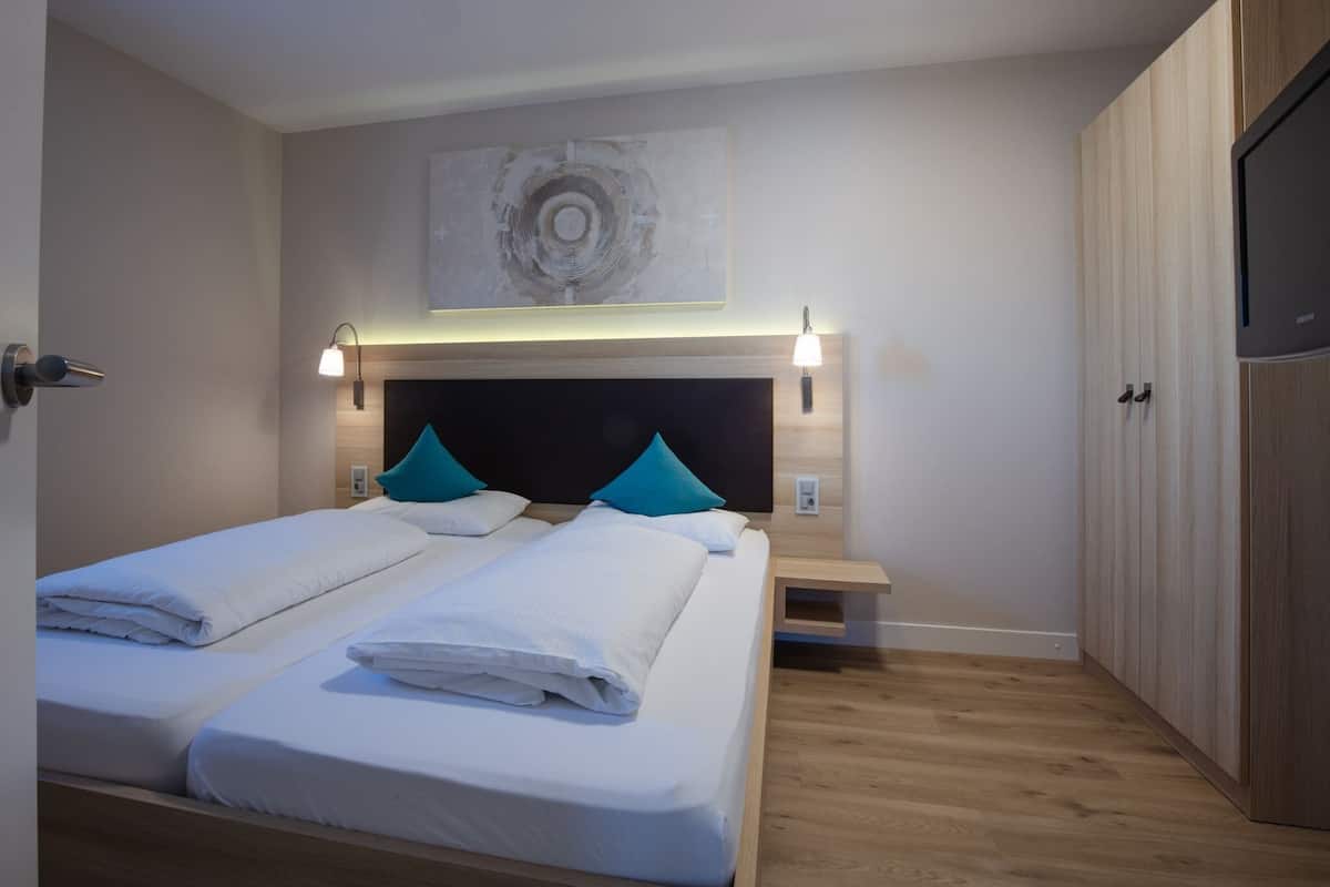 A modern hotel room with two beds, a wooden headboard, a flat-screen TV, and a painting on the wall.