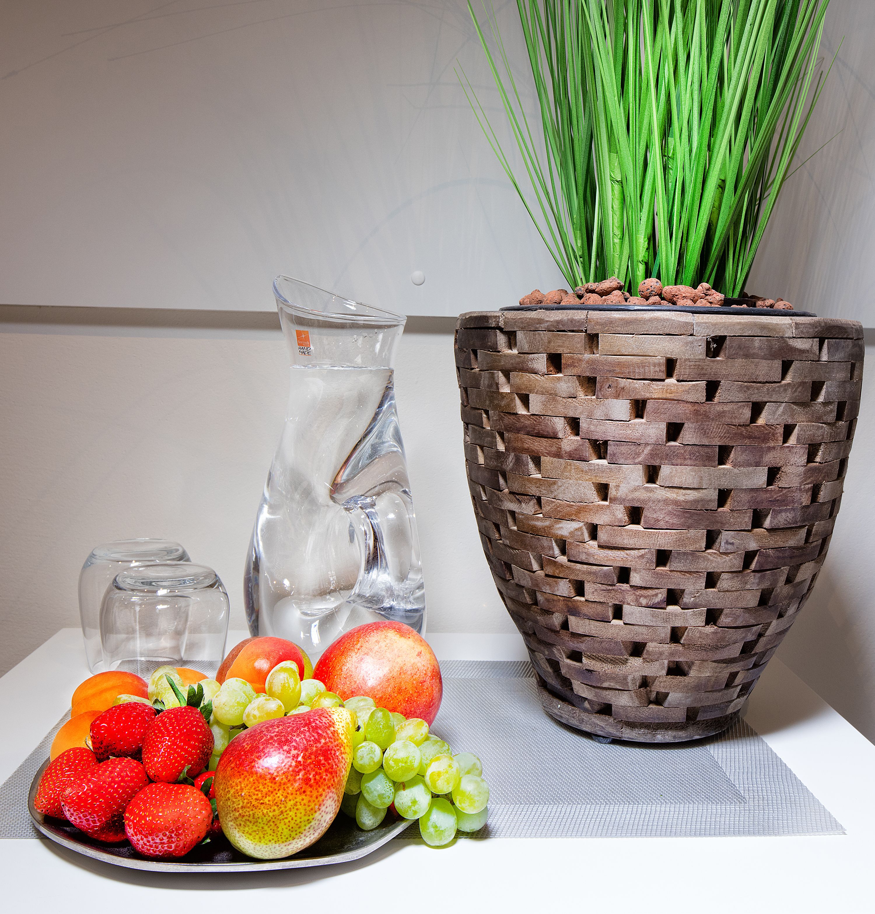 A table with a fruit bowl, a pitcher, and a potted plant.