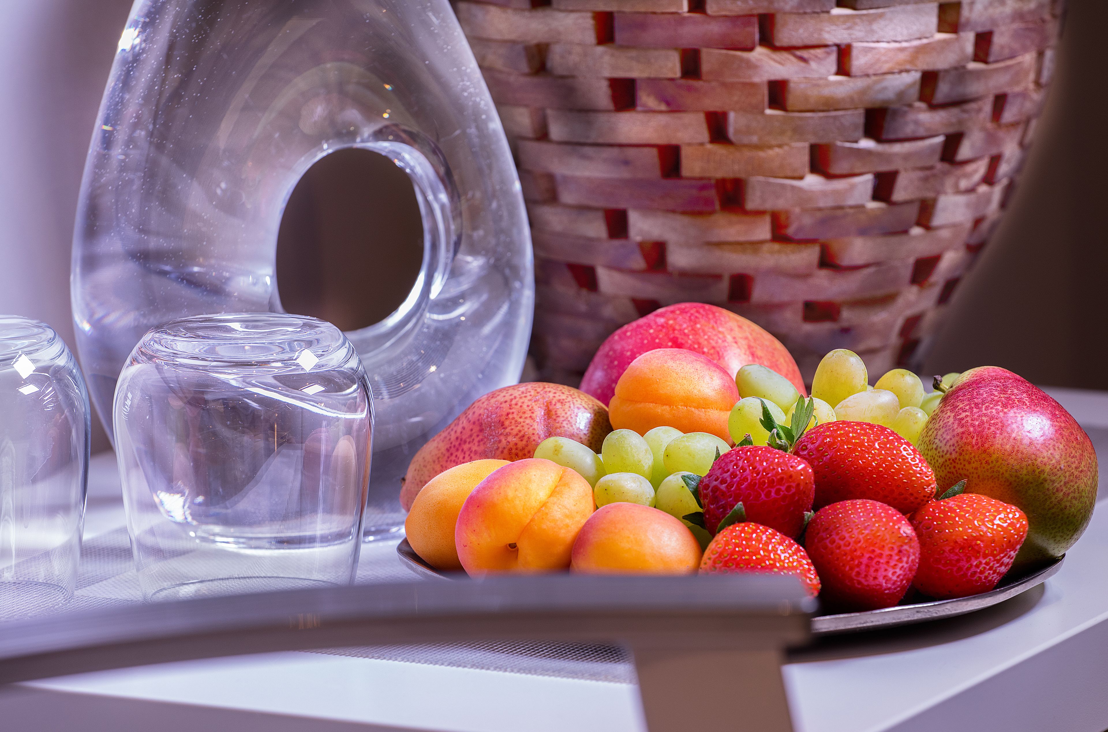A fruit bowl with various fruits, a clear glass vase, and a woven basket.