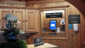 Un comptoir d’accueil en bois avec une pancarte indiquant « Enregistrement ». On y trouve un écran d’ordinateur, un distributeur de gel hydroalcoolique et une pancarte avec le texte « Herzlich Willkommen Welcome ».