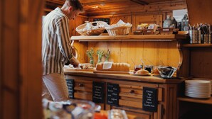 Un comptoir de boulangerie où l’on trouve du pain, des pâtisseries, et un tableau noir affichant le menu avec des articles tels que du fromage, du beurre et du lait.
