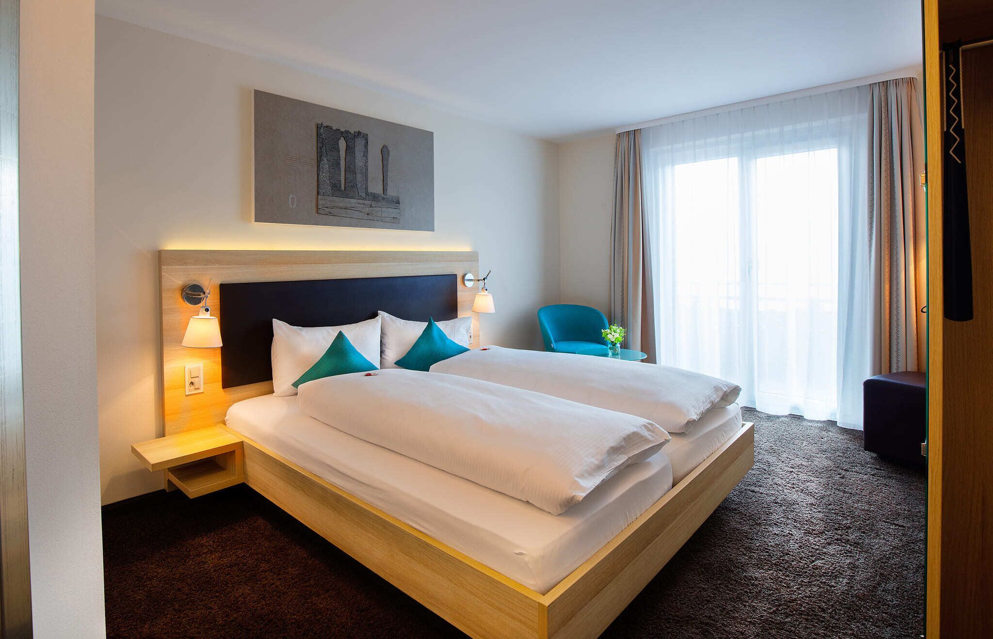 Een hotelkamer met een groot bed, twee nachtkastjes, een stoel, een raam met gordijnen en een schilderij aan de muur.