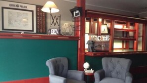 Une pièce comprenant deux fauteuils gris, une lampe, un tableau encadré, une pancarte de bienvenue et une étagère ornée d’objets décoratifs.